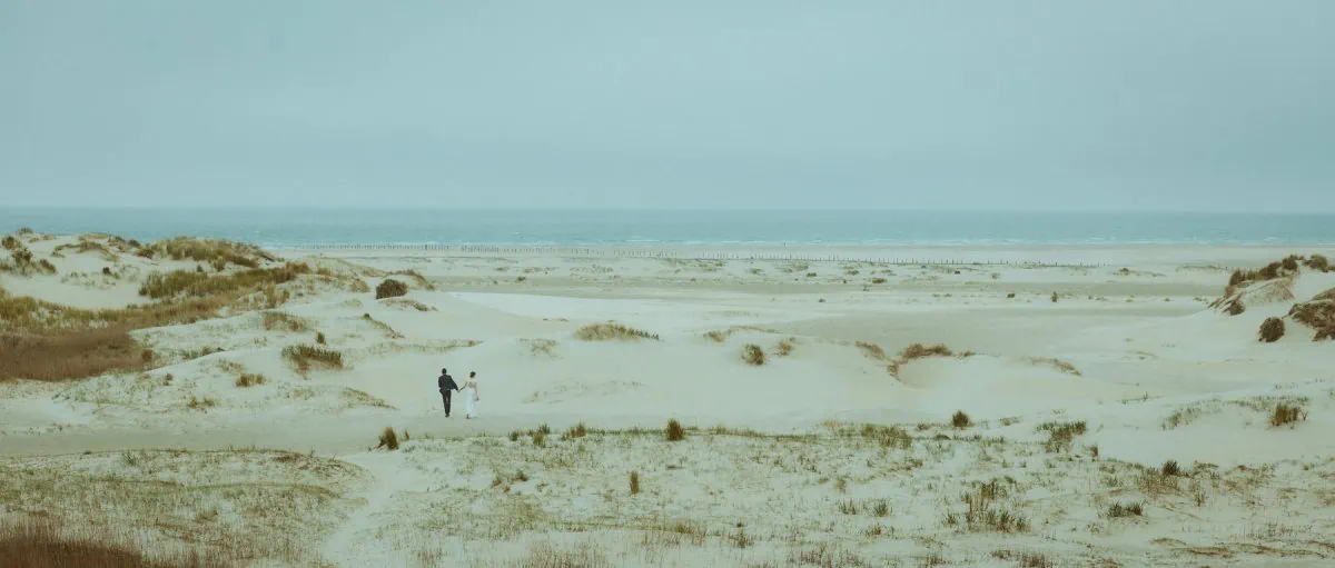 A couple eloping at the North Sea, walking hand in hand through the quiet, endless dunes of Rømø. A raw, intimate moment in nature—just the two of them, surrounded by wind, sand, and stillness.