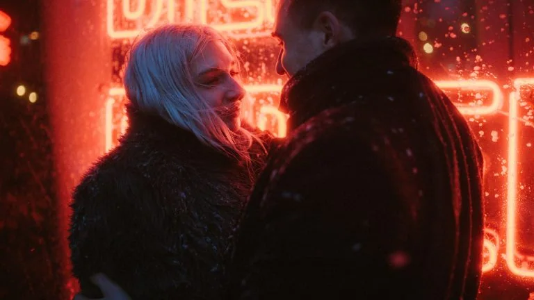 a man and woman standing in front of a neon sign
