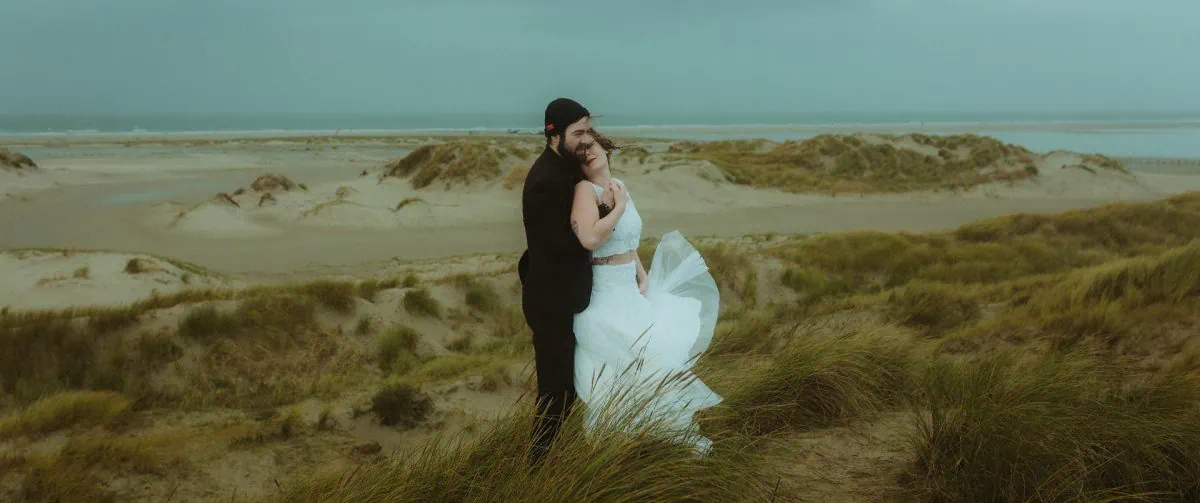 Elopement auf Rømø: Ein Paar umarmt sich auf einer windumtosten Düne mit Blick auf die wilde Nordsee. Ihr Kleid tanzt im stürmischen Wind – intim, echt und voller roher Nordsee-Atmosphäre. Der perfekte Ort für eine freie Trauung am Meer.